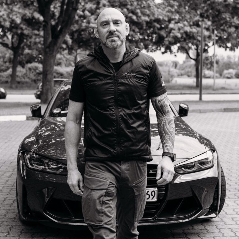 Schwarz-weiß Foto von Dr. Alexander Madaus mit Auto im Hintergrund